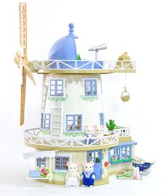 a doll house is shown with the roof and windows painted blue, while two bears are standing in front of it