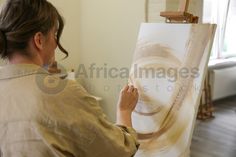 a woman is painting on an easel in her living room while looking at it