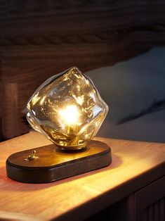 a glass lamp sitting on top of a wooden table next to a night stand with a bed in the background