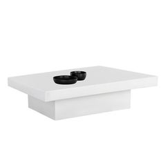 a white coffee table with two black bowls on it's center piece and an empty shelf below