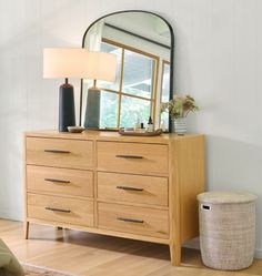 a dresser with a mirror, lamp and basket on the floor in front of it