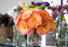 a vase filled with orange and pink flowers on top of a glass table in front of a mirror