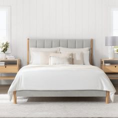 a bed with white sheets and pillows in a bedroom next to two nightstands on either side of the bed