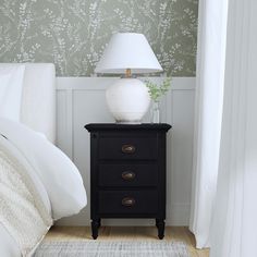 a night stand with a lamp on it next to a bed