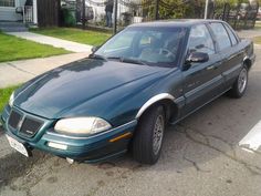 a green car is parked on the side of the road in front of a house