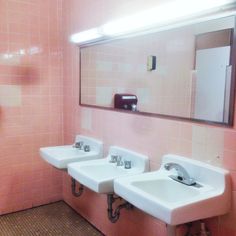 three sinks in a bathroom with pink tiles on the walls and brown wood flooring