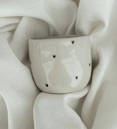 a white cup sitting on top of a table covered in sheets and cloths with hearts drawn on it