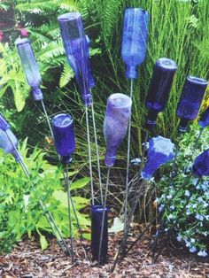 there are many blue glass vases in the ground near some plants and flowers,