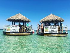 two boats with thatched roofs are in the clear blue water, while people stand on top of them