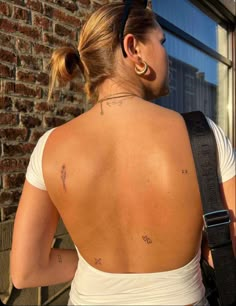 a woman with tattoos on her back standing in front of a brick wall and looking out the window