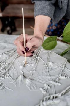 a woman is working on a sculpture with a wooden stick in her hand and some flowers behind her