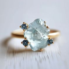 an aquamarine and blue diamond ring on a white surface with gold trimmings