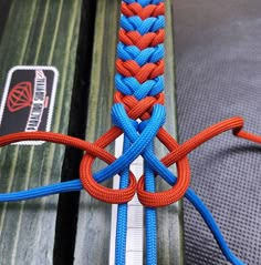 an orange and blue rope is attached to a bench with another piece of wood in the background