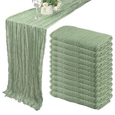 a stack of green cloths next to a vase with flowers and wine glasses on it