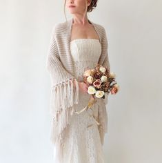 a woman in a white dress holding a bouquet of flowers and wearing a shawl