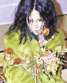 a woman in a green fur coat holding flowers