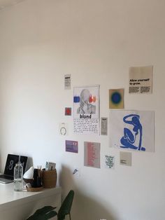 a white desk topped with a laptop computer next to a wall covered in pictures and papers