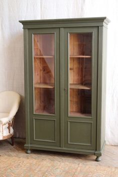 a green cabinet with glass doors next to a chair