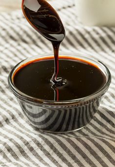 a spoon pouring sauce into a bowl on top of a striped table cloth with a white vase in the background