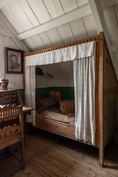 an old fashioned bed in a room with wood flooring and white curtains on the windowsill