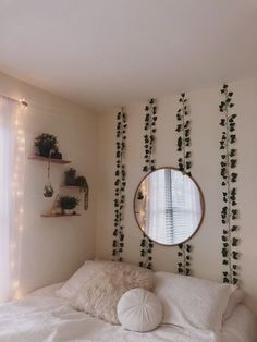 a bedroom with white bedding and green plants on the wall, along with a round mirror