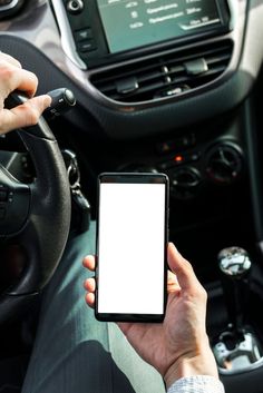 a person holding a cell phone in their hand while sitting in a car with the steering wheel behind them