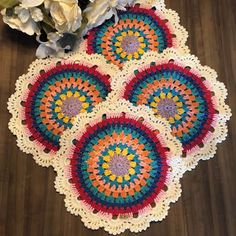 four crocheted doily on a table with flowers