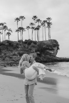 a man carrying a pregnant woman on the beach with palm trees in the back ground