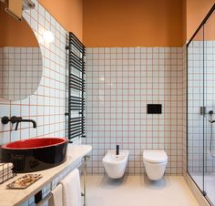 a bathroom with two toilets and a red bowl on the toilet seat in front of it