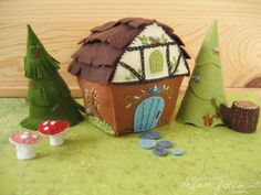 a small house made out of felt with trees and mushrooms on the ground next to it