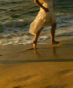 a woman in white dress walking on beach next to ocean