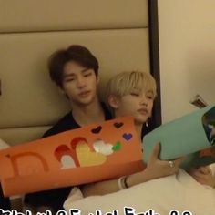 two boys are sitting on a bed and one boy is holding a large cardboard box