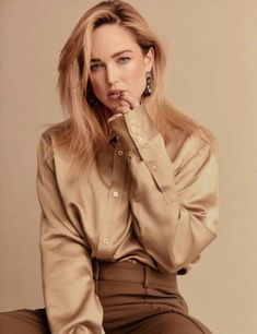 a woman sitting on top of a stool with her hand to her mouth and looking at the camera