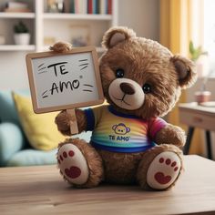 a brown teddy bear sitting on top of a table holding a sign that says te amo