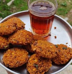 a metal tray with some cookies and a cup of tea on it next to grass