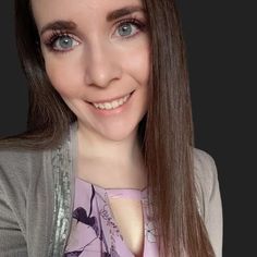 a woman with long brown hair and blue eyes smiles at the camera while wearing a gray cardigan