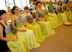 a group of women sitting next to each other in front of a table filled with green cloths