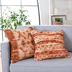 two orange and white pillows sitting on top of a blue couch in front of a window