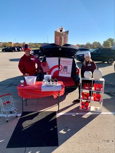 two women standing next to a table with food on it in front of a car