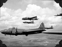 four airplanes flying in formation over the ocean and land below them on a cloudy day