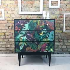 a black and green painted dresser sitting in front of a brick wall with pictures on it