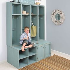 a young boy sitting on top of a blue bookcase next to a wall mounted clock