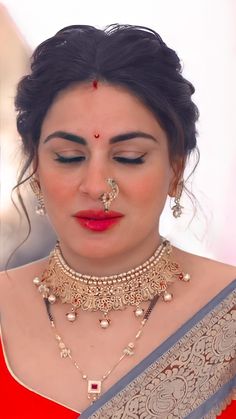 a woman in a red sari with jewelry on her neck and nosepieces