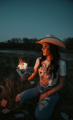 a woman wearing a cowboy hat sitting on the ground with playing cards in her hand