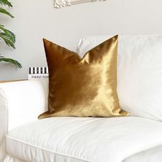 a gold pillow sitting on top of a white couch next to a potted plant