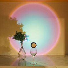 two wine glasses and a vase with flowers in front of a rainbow colored wallpaper