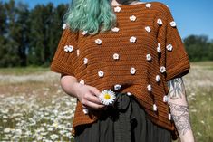 a woman with green hair wearing a brown sweater and holding a daisy in her hand