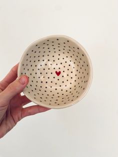 a hand holding a white bowl with black dots and a red heart