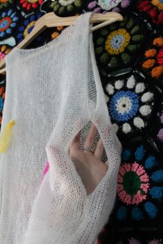 a person's hand on top of a piece of white knitted material with colorful flowers