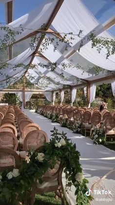 an outdoor wedding venue set up with white drapes and greenery on the ceiling